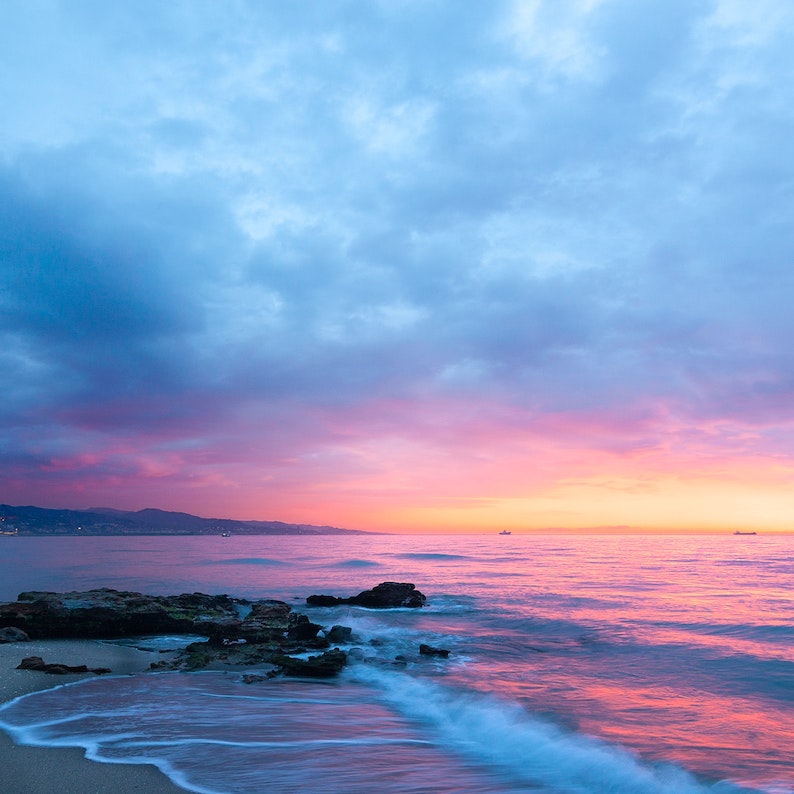 Calm water gently lapping shoreline under blue, pink and yellow sky